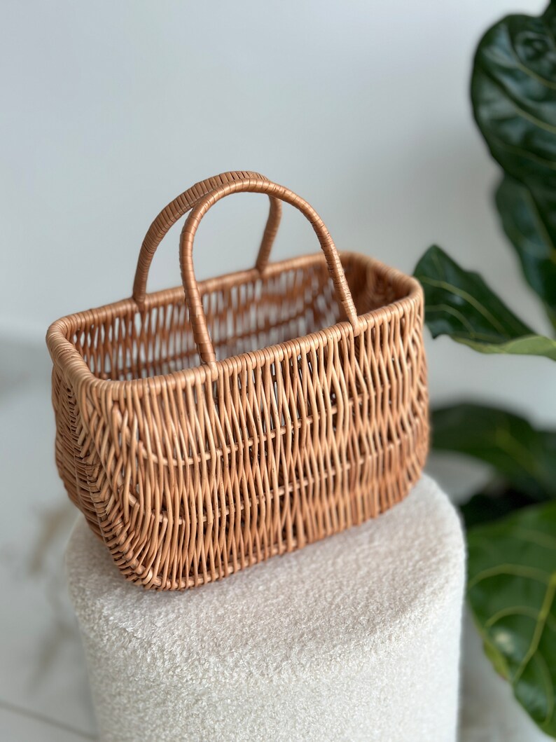 May include: A woven wicker basket with a rectangular shape and a single handle. The basket is light brown and has a natural, rustic look.