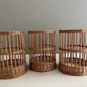 Puede incluir: Tres cestas cil&iacute;ndricas hechas de mimbre marr&oacute;n natural. Cada cesta presenta una base tejida, listones verticales que forman los lados y una banda horizontal reforzada alrededor del centro, creando una estructura abierta y aireada.