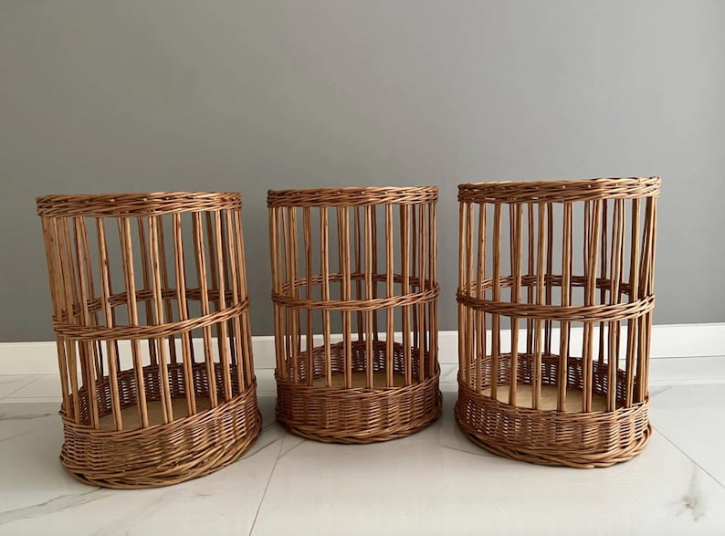Puede incluir: Tres cestas cil&iacute;ndricas hechas de mimbre marr&oacute;n natural. Cada cesta presenta una base tejida, listones verticales que forman los lados y una banda horizontal reforzada alrededor del centro, creando una estructura abierta y aireada.