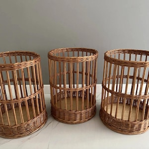 Puede incluir: Tres cestas cil&iacute;ndricas fabricadas en mimbre marr&oacute;n natural. Cada cesta presenta un dise&ntilde;o de listones verticales con una base tejida reforzada y un fondo plano de madera clara. Los recipientes abiertos tienen una estructura uniforme.