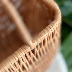 May include: Close-up of a woven wicker basket with a natural brown color. The basket is made of thin, tightly woven strips of rattan.