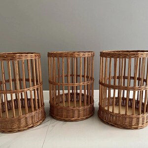 Puede incluir: Tres cestas cil&iacute;ndricas fabricadas en mimbre marr&oacute;n natural. Cada cesta presenta una base tejida, listones verticales que forman los lados y una banda horizontal reforzada en el medio, creando una estructura abierta tipo jaula.