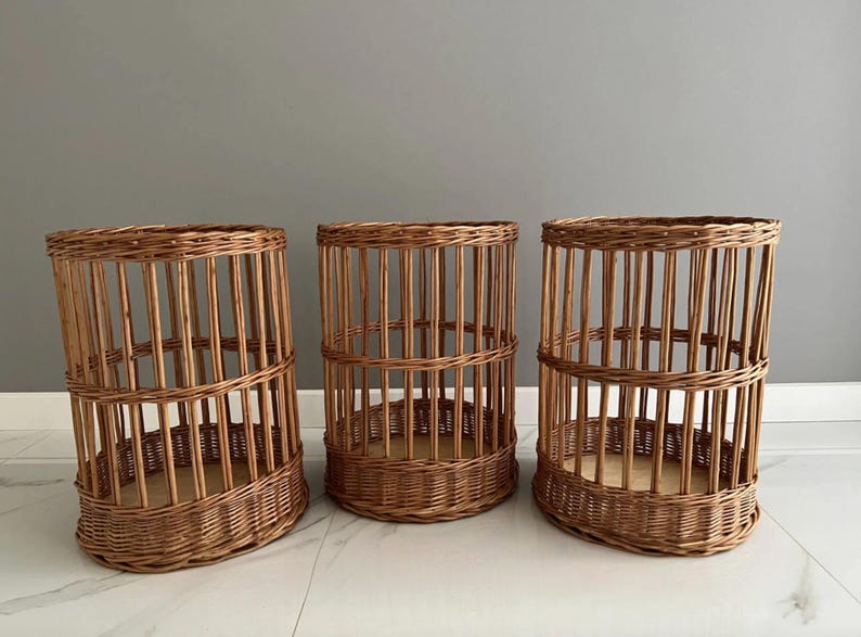 Puede incluir: Tres cestas cil&iacute;ndricas fabricadas en mimbre marr&oacute;n natural. Cada cesta presenta una base tejida, listones verticales que forman los lados y una banda horizontal reforzada en el medio, creando una estructura abierta tipo jaula.
