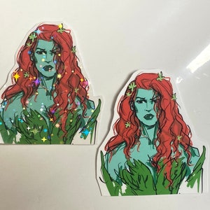 Op de afbeelding: Twee stickers met een vrouw met groene huid, rood haar en groene wijnstokken. De vrouw heeft een strenge uitdrukking en draagt een groene, bladerrijke outfit. De sticker links heeft een holografische afwerking.