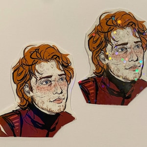 May include: Two stickers of a cartoon illustration of a person with red hair, freckles, and a red and black outfit. The stickers have a holographic finish.