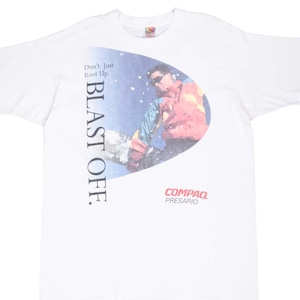 May include: White t-shirt with a graphic featuring a person wearing sunglasses and a colorful jacket, set against a blue and white background. The text "BLAST OFF." is printed vertically on the left side, with "COMPAQ PRESARIO" at the bottom.