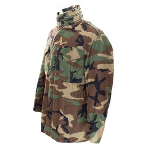 May include: Camouflage pattern jacket with a stand-up collar and multiple front pockets. The jacket features a mix of green, brown, and black hues, typical of military-style apparel. The jacket is made of a durable fabric.