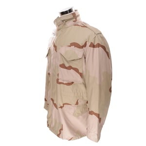 May include: A tan and brown camouflage jacket with a high collar and multiple pockets. The jacket is made of a durable material and features a zipper closure. The jacket is displayed on a mannequin.