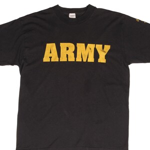 Pode incluir: Uma t-shirt preta de manga curta com a palavra ARMY impressa em letras maiúsculas grandes, a negrito e amarelas no peito. A peça tem um decote redondo padrão e um corte descontraído, com um pequeno detalhe gráfico amarelo na manga esquerda.