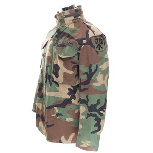 May include: Camouflage pattern jacket with the text "U.S. ARMY" on the pocket. The jacket features a high collar, multiple pockets, and a zipper closure. The color palette includes shades of green, brown, and black.