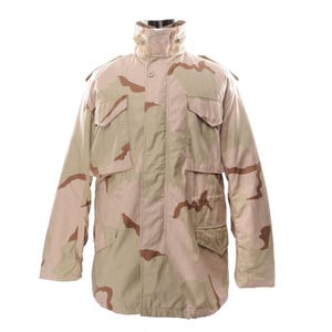 May include: A tan and brown camouflage military jacket with multiple pockets and a high collar. The jacket has a button-up front and epaulets on the shoulders. The jacket is made of a durable material.