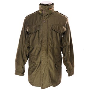 May include: An olive green military-style jacket with multiple pockets and a high collar. The jacket has a button and zip closure, epaulettes, and a lined interior. The sleeves are long, and the jacket has a classic, utilitarian design.