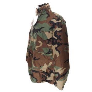 May include: Camouflage pattern jacket with a high collar and multiple front pockets. The jacket features a zipper closure and a woodland camouflage design in shades of green, brown, and black. The jacket is displayed on a mannequin.