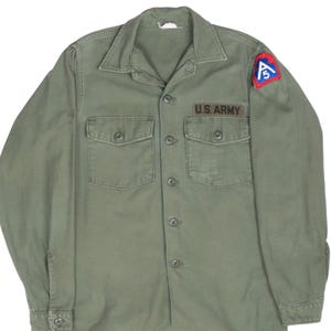 Peut inclure: Une chemise à manches longues vert olive avec deux poches de poitrine et une fermeture boutonnée. La chemise comporte un écusson "U.S. ARMY" et un écusson coloré sur la manche supérieure. Style militaire classique.