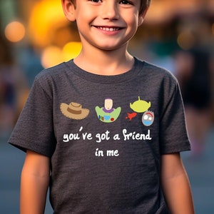 May include: A dark grey t-shirt with a graphic of the Toy Story characters Woody, Buzz Lightyear, and Alien. The text "you've got a friend in me" is printed below the graphic.