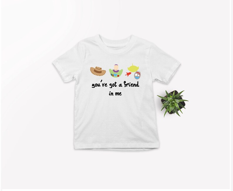 May include: White t-shirt with a graphic of characters from the movie Toy Story. The graphic includes Woody's hat, Buzz Lightyear, a spaceship, and a toy alien. The text "you've got a friend in me" is printed below the graphic.
