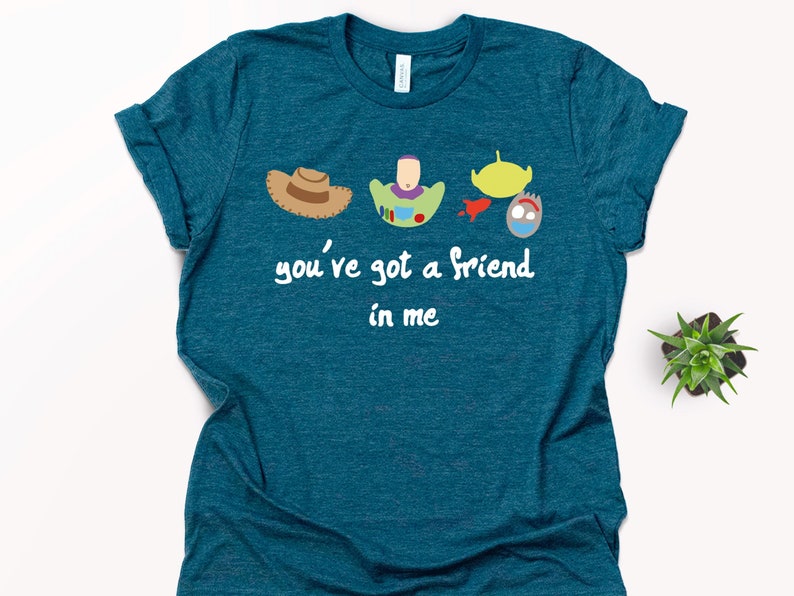 May include: Teal blue t-shirt with a white graphic of the Toy Story characters Woody, Buzz Lightyear, Alien, and Rex. The text "you've got a friend in me" is printed below the characters.