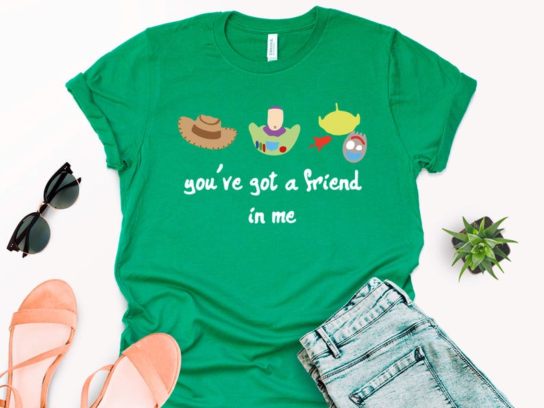 May include: Green t-shirt with a white graphic of characters from the Toy Story movie. The graphic includes Woody, Buzz Lightyear, and the alien. The text on the shirt reads "you've got a friend in me."