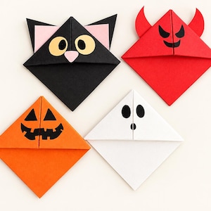 May include: Four triangular paper corner bookmarks featuring character designs. One is a black cat with yellow eyes and pink ears, one is a red devil with horns, one is an orange jack-o'-lantern with a black face, and one is a white ghost with black eyes.