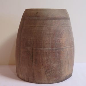 Puede incluir: Un recipiente de madera redondo en forma de barril, de color marrón, con una superficie lisa y una parte superior ligeramente acampanada.