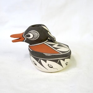 May include: A handcrafted ceramic duck figurine with a black head and body, a red beak, and a white belly. The duck is decorated with geometric patterns in black and white. The figurine is likely a decorative item or a small container.