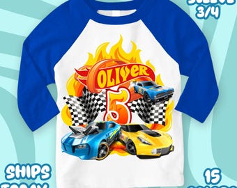 May include: A white and blue raglan-style shirt with a race car theme. The shirt features a graphic with the name "Oliver" and the number "5", along with illustrations of race cars, flames, and checkered flags. The sleeves are blue.