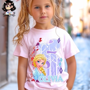 Puede incluir: Una camiseta rosa claro con un gr&aacute;fico de Elsa de Frozen, el n&uacute;mero 5 y el nombre "Olivia" en azul claro. El dise&ntilde;o incluye copos de nieve y una escena de bosque. La camiseta la lleva una ni&ntilde;a.