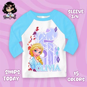 Puede incluir: Camiseta blanca y azul claro con mangas ragl&aacute;n con un gr&aacute;fico de Elsa de Frozen. El dise&ntilde;o incluye el nombre "Olivia" y el n&uacute;mero "5" con un fondo de bosque invernal. La camiseta tiene mangas 3/4.