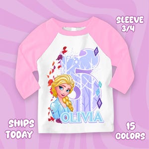 Puede incluir: Una camiseta de manga ragl&aacute;n blanca y rosa con una imagen de dibujos animados de Elsa de Frozen. La camiseta tiene un gran n&uacute;mero 5 con un dise&ntilde;o de bosque invernal, el nombre "OLIVIA" y el texto "SLEEVE 3/4".