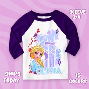 Puede incluir: Camiseta de estilo ragl&aacute;n blanca y morada con una imagen de dibujos animados de una mujer rubia con el nombre "Olivia" y el n&uacute;mero "5". La camiseta tiene mangas 3/4 y el texto "15 COLORES".