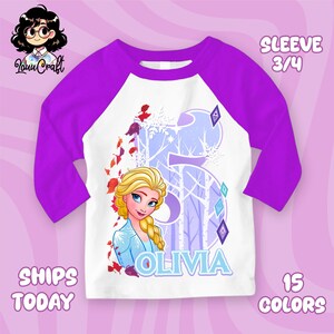 Puede incluir: Una camiseta de estilo ragl&aacute;n blanca y morada con una imagen de dibujos animados de Elsa de Frozen. La camiseta tiene mangas 3/4 y el nombre "Olivia" impreso en la parte delantera. El n&uacute;mero "5" tambi&eacute;n aparece.
