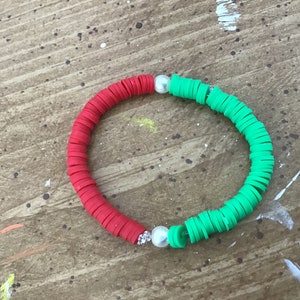 May include: A red and green beaded bracelet with two white pearl accents.