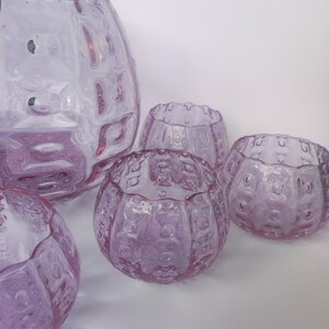 May include: Set of five clear, lavender-coloured glass bowls with a textured, bubble-like design. The bowls are arranged in a semi-circle on a white surface.