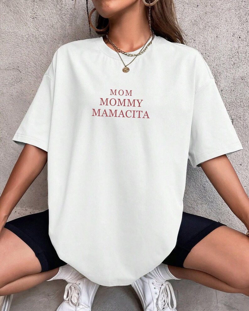 Pu&ograve; includere: T-shirt bianco a maniche corte con le parole "MOM MOMMY MAMACITA" stampate in rosso. La maglietta &egrave; in stile casual, adatta per l'uso quotidiano.