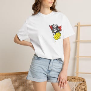 Könnte beinhalten: Ein weißes Kurzarm-T-Shirt mit einem Aufdruck auf der linken Brust. Die Grafik zeigt eine Comic-Figur mit Maske, die eine rote Flagge hält, sowie eine gelbe Sprechblase mit dem Text: My super power: spotting red flags early.