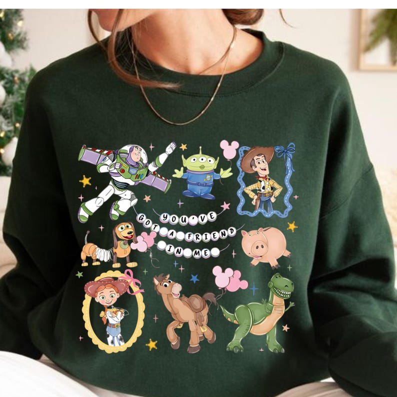 Puede incluir: Sudadera verde oscuro con un gr&aacute;fico colorido de personajes de una popular pel&iacute;cula de animaci&oacute;n. El dise&ntilde;o incluye a Buzz Lightyear, Woody, un extraterrestre y otros personajes, con el texto "You've Got a Friend in Me".