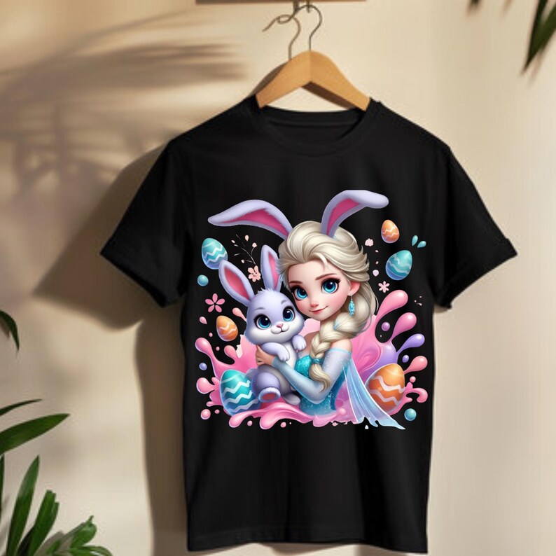 May include: Black t-shirt featuring a cartoon illustration of a princess with bunny ears hugging a purple bunny. The design includes colorful Easter eggs and a pink splash background.