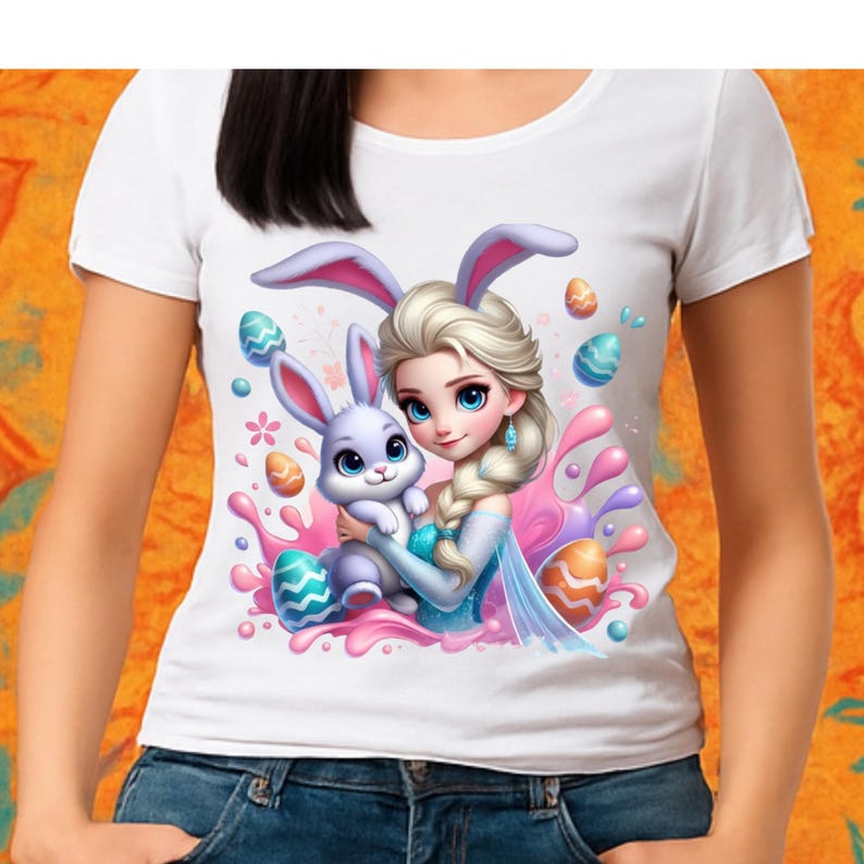 May include: White t-shirt featuring a cartoon illustration of a princess with a bunny, Easter eggs, and colorful splashes. The princess has blonde hair and is wearing a blue dress. The bunny is light purple. The design is centered on the shirt.
