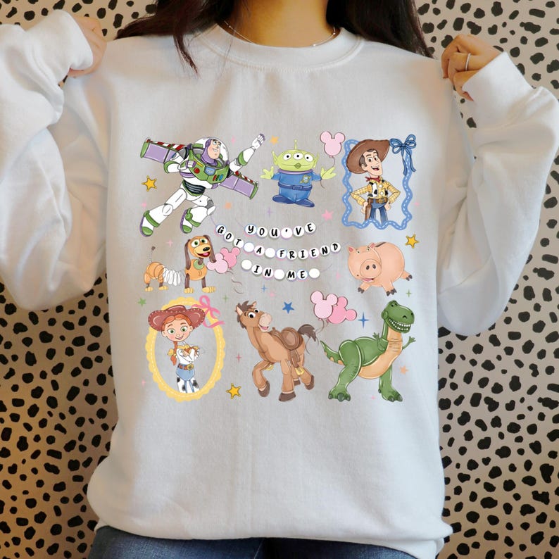 Puede incluir: Sudadera blanca con personajes de dibujos animados coloridos de una popular pel&iacute;cula animada. El dise&ntilde;o incluye a Buzz Lightyear, un extraterrestre, Woody, Jessie, Slinky Dog, Hamm, Bullseye y Rex. Tambi&eacute;n se muestra el texto "You've Got a Friend in Me".