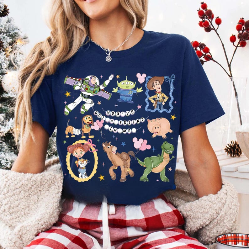 Puede incluir: Camiseta azul marino con personajes de dibujos animados coloridos. La camiseta muestra el texto "You've Got A Friend In Me" e im&aacute;genes de un guardabosques espacial, un vaquero y otros personajes.