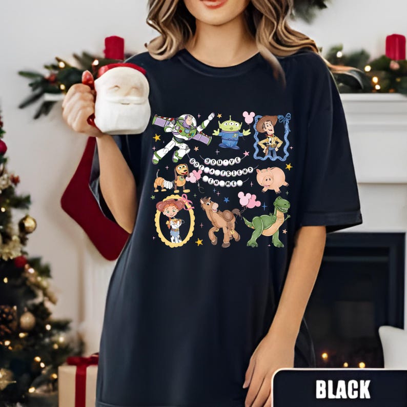 Puede incluir: Camiseta negra con gr&aacute;ficos de personajes de dibujos animados coloridos. El dise&ntilde;o incluye im&aacute;genes de un guardabosques espacial, un extraterrestre, una vaquera, un cerdo, un dinosaurio, un caballo y un perro. La palabra "BLACK" se muestra en la parte inferior de la imagen.