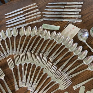 Puede incluir: Un juego de cubiertos de plata, que incluye cucharas, tenedores y cuchillos. Los cubiertos están dispuestos sobre una mesa de madera. Los cubiertos tienen un diseño adornado.