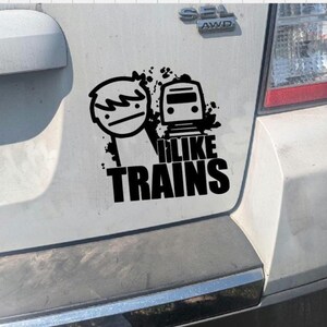May include: Black and white sticker featuring a stick figure with a train and the text "I LIKE TRAINS". The sticker is applied to the rear of a vehicle.