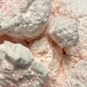 Puede incluir: Primer plano de una sustancia esponjosa blanca y rosa con textura granulada. La sustancia está en un recipiente transparente.