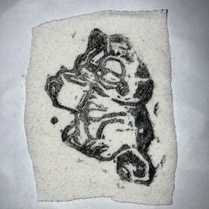 May include: Black and white illustration of a cartoon dog printed on a white fabric patch.