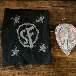 May include: A black fabric with a white "SF" logo and four white stars. A pink rubber stamp with a white "SF" logo.