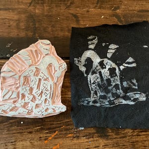 May include: A pink rubber stamp with a detailed design of a creature with a checkered pattern. The stamp is used to create a white print on a black fabric.