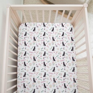 May include: A white fitted crib sheet with a repeating pattern of black dogs and pink flowers. The sheet has the name "Harper" printed on it.