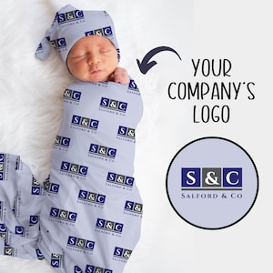 May include: A light blue baby swaddle with a repeating pattern of the text "S&C Salford & Co." in dark blue and gray. The swaddle is wrapped around a baby wearing a matching hat. The text "YOUR COMPANY'S LOGO" is written in black above a circle with the text "S&C Salford & Co." in dark blue and gray.