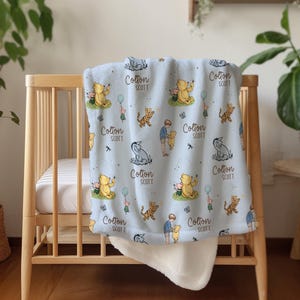 May include: A light blue baby blanket with a repeating pattern of cartoon characters, including a bear, tiger, and boy. The blanket is draped over a wooden crib. The text "Cotton SCOTT" is printed on the blanket.